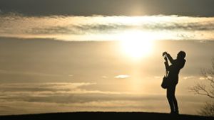 Eine Frau macht ein Selfie, während im Hintergrund die Sonne untergeht.